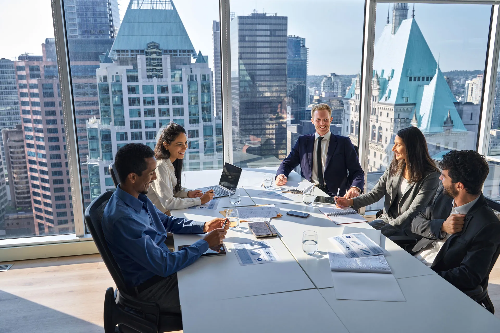 A group of business people seated at a table, engaged in discussion, with a large window in the background