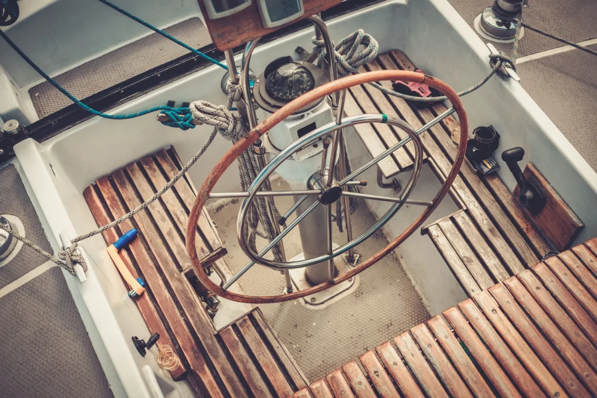 A boat's steering wheel surrounded by a polished wooden deck